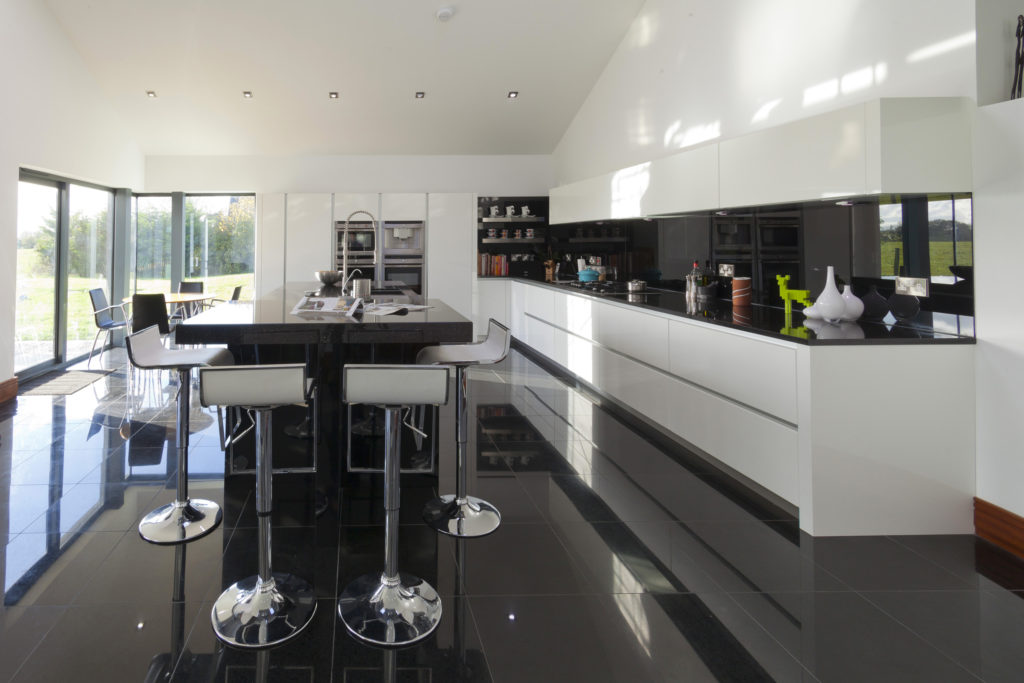 A black and white kitchen, designed in a modern style. The floor is black, and the cabinets are white with a black, quartz counter top.
